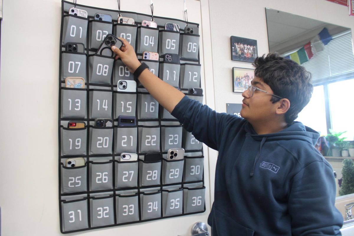 A student putting his phone in his teachers phone caddy.