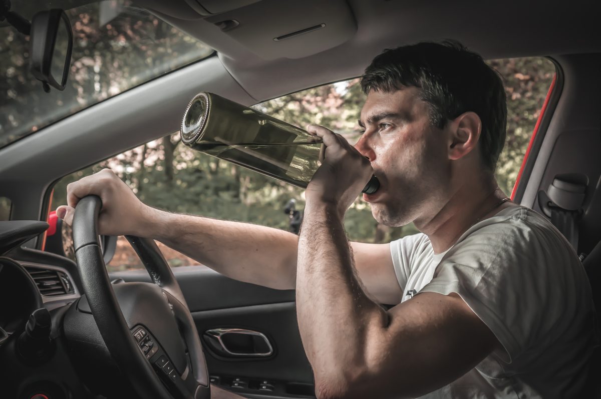Drunk driver with bottle of wine driving a car - vehicle, alcohol and driving concept
